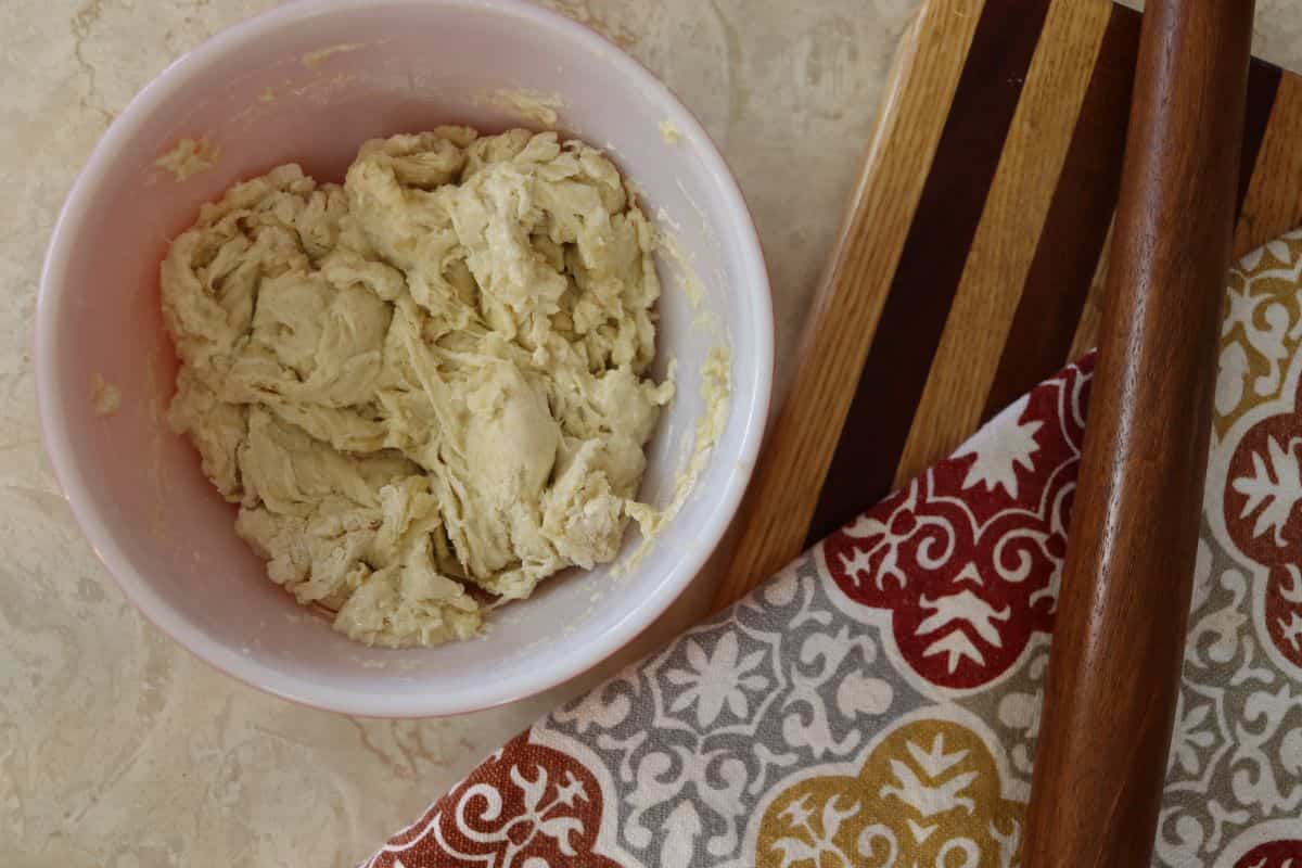 Shaggy dough in a white bowl sitting next to a striped cutting board and a napkin with a red, grey, and yellow pattern on it.