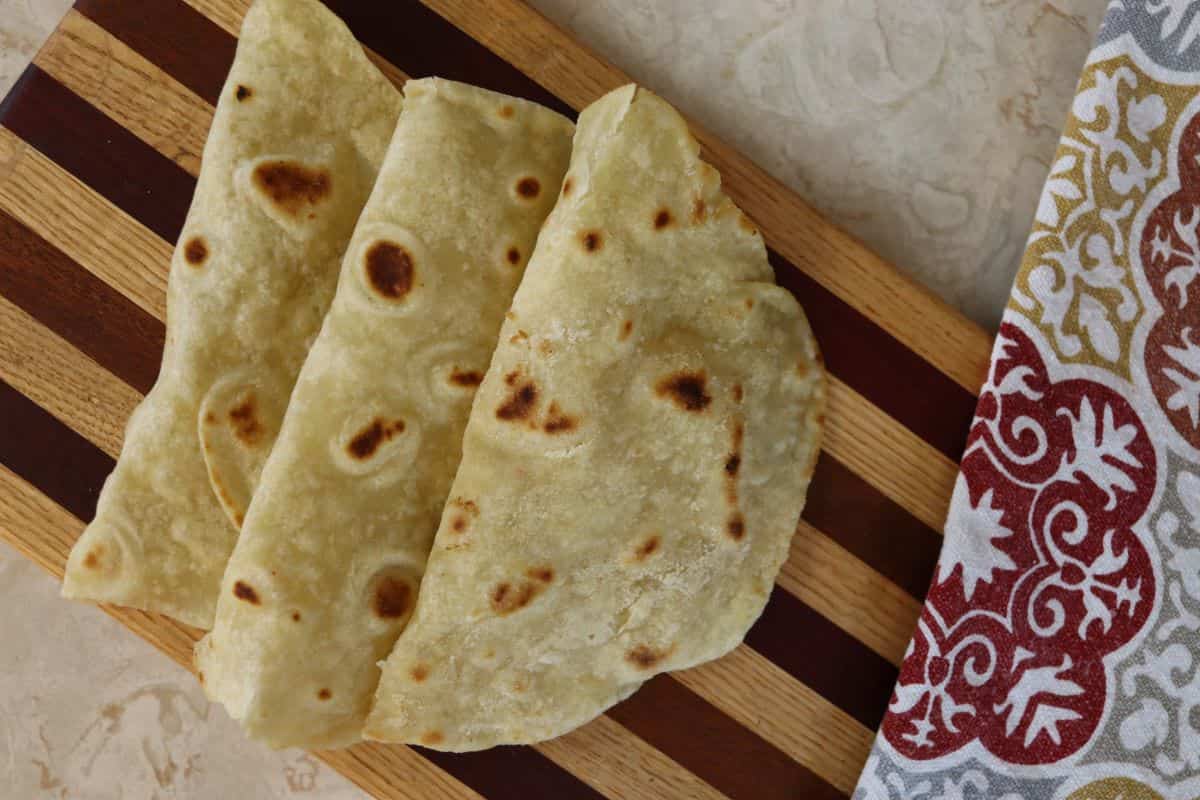 homemade tortilla shells folded in half and laid out on a striped cuttting board.
