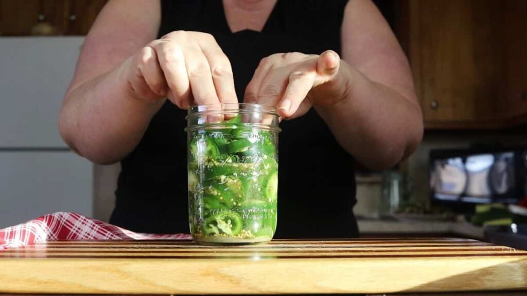 woman packing jalapenos in a canning jar