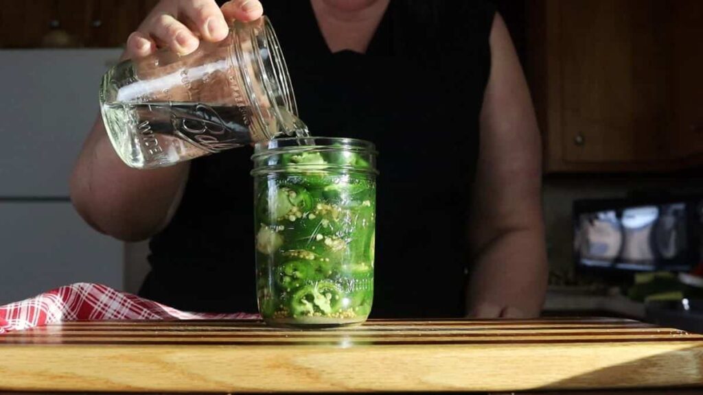 woman pouring vinegar into a jar of jalapenos