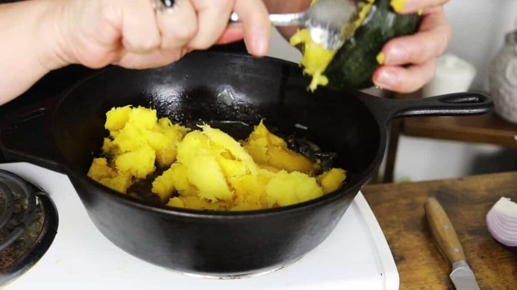 scooping flesh from squash into a pot for acorn squash soup