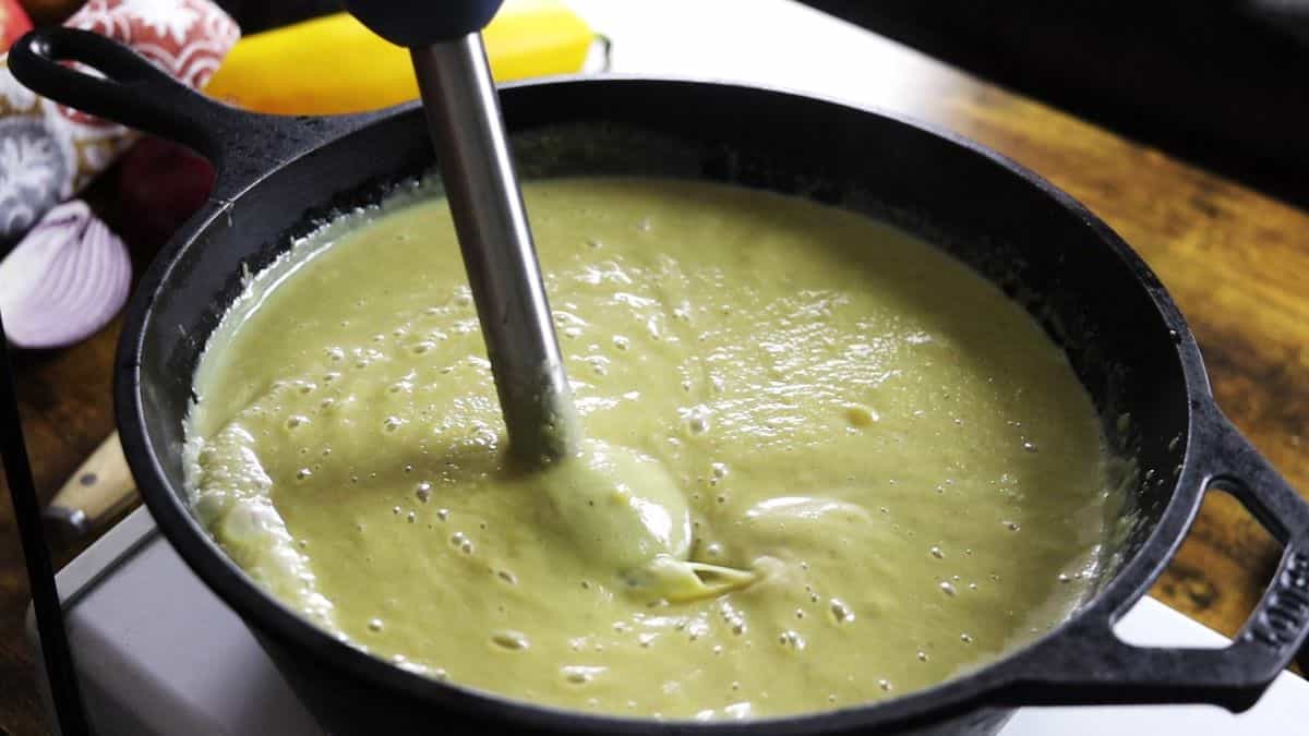 An immersion blender immersed in a pot of creamy soup.