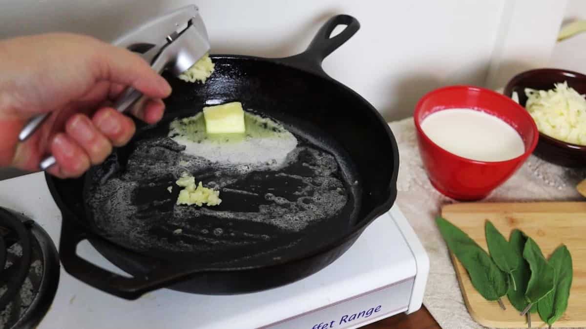 Pressing garlic into a cast iron skillet of melting butter on a stovetop.