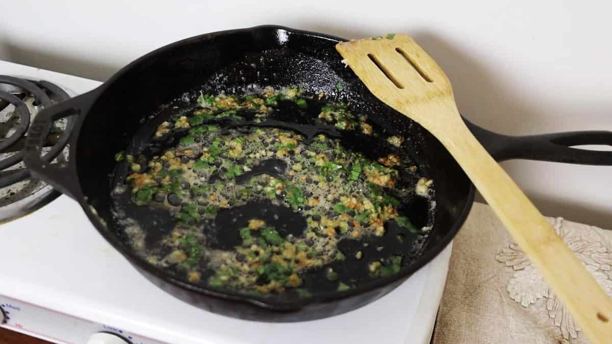 Garlic and sage simmering in a cast iron skillet with a wooden spoon resting on the skillet.