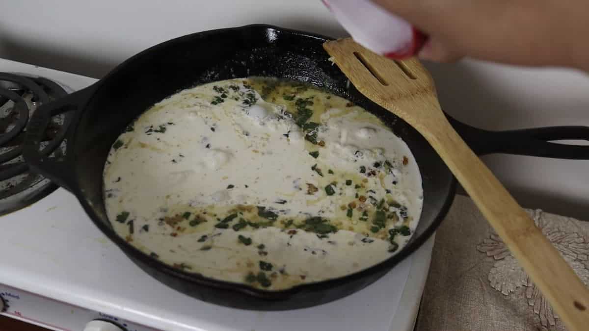 Cream, garlic, and sage simmering in a cast iron skillet with a wooden spoon resting on the edge. 
