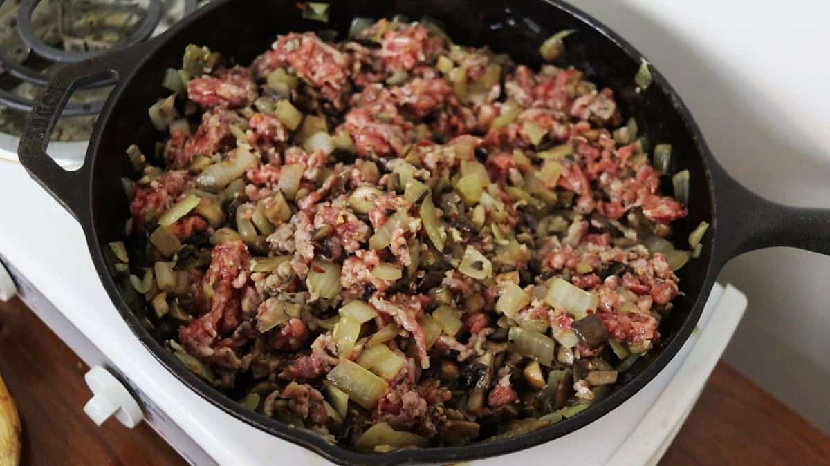 Raw sausage mixed together with cooked mushrooms and onions in a cast iron skillet.