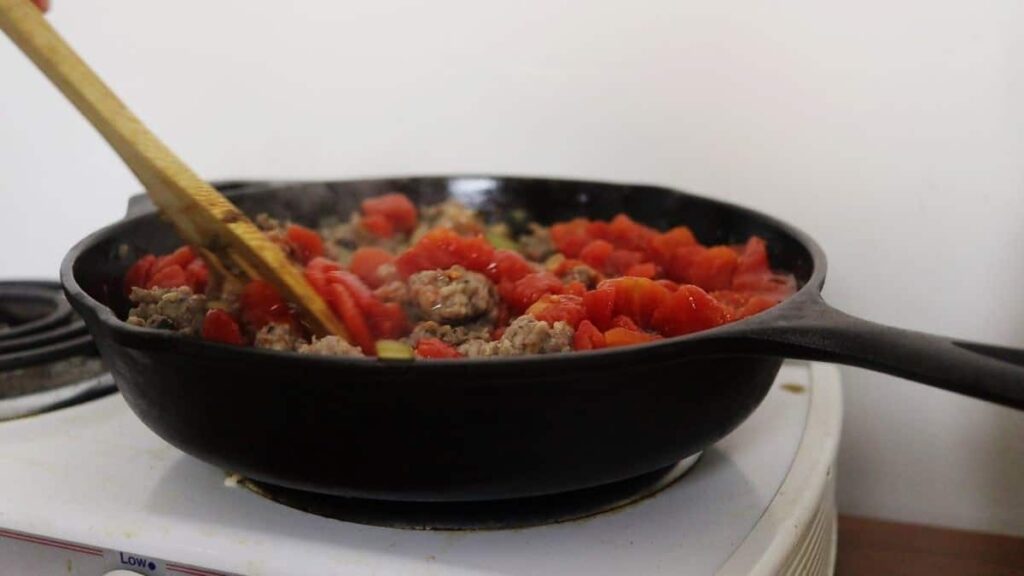 stirring tomatoes into a recipe in a cast iron skillet