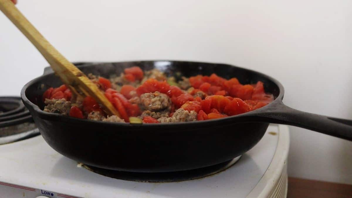 Sausage and chopped tomatoes in a cast iron skillet on a stovetop.