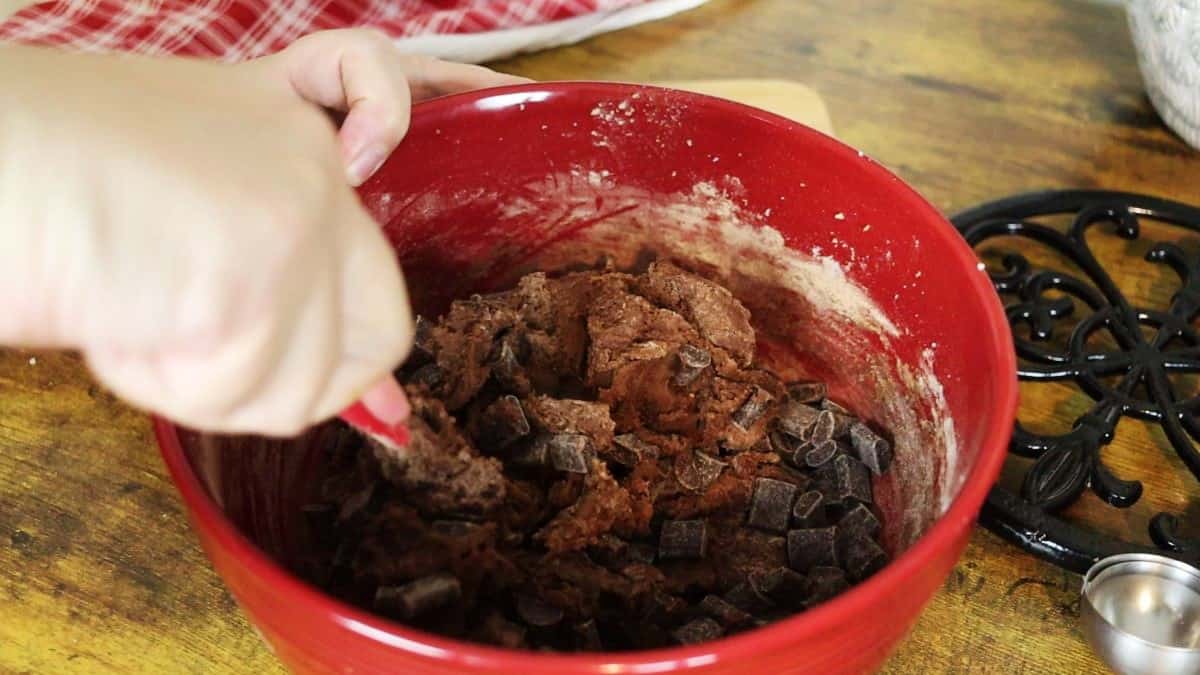 Dark brown batter with chocolate chunks being stirred in a red bowl.