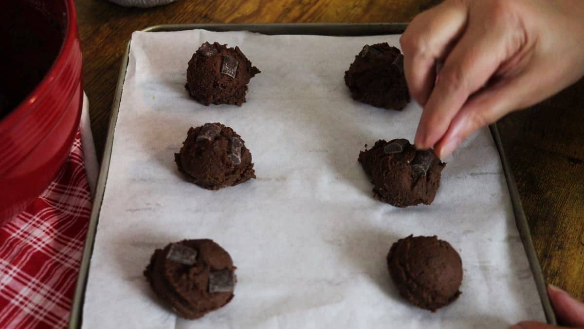 Scoops of dark brown batter on a parchment lined baking sheet.
