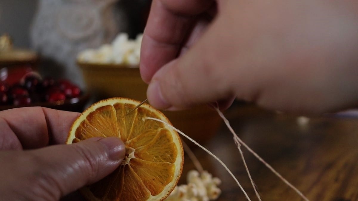 Hands threading hemp cord through a dried orange slice.