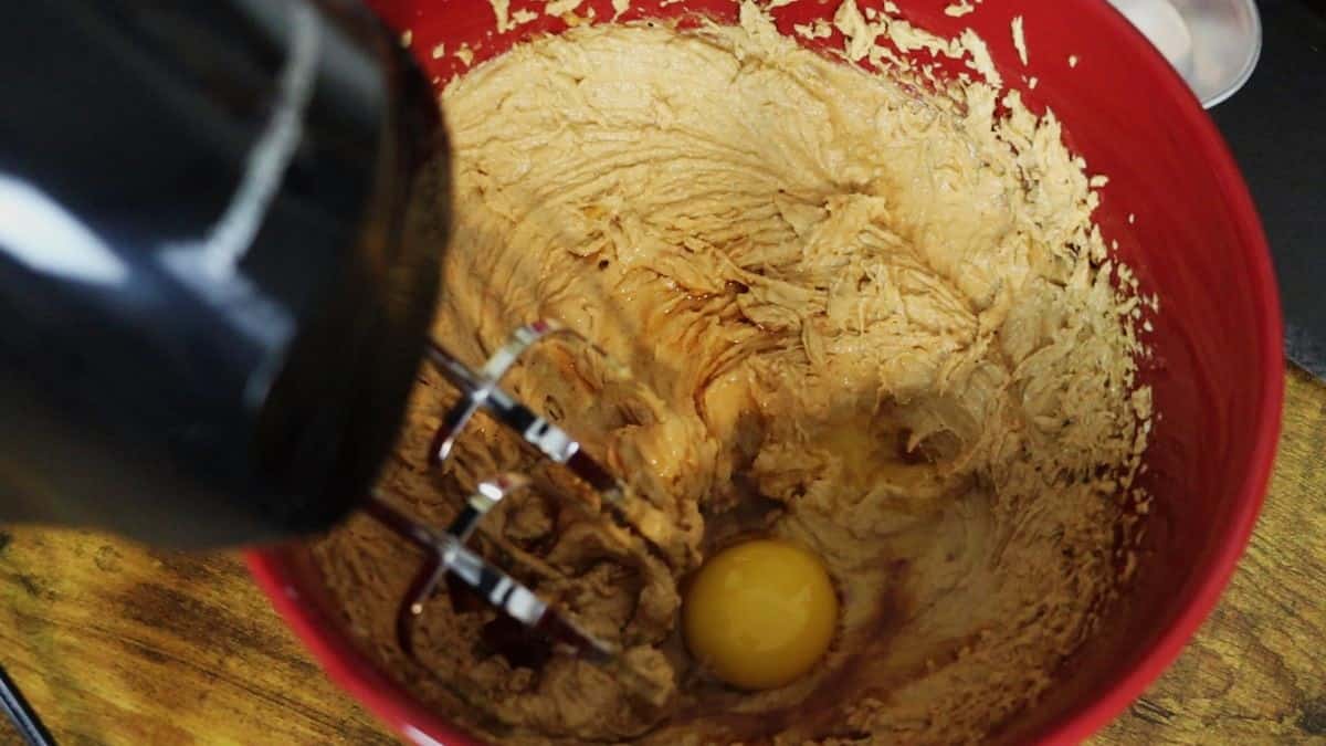 Beaters in a bowl of light brown batter with an egg visible in the bowl.
