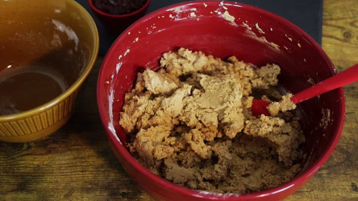 Light brown cookie batter in a red bowl sitting on a wooden table.