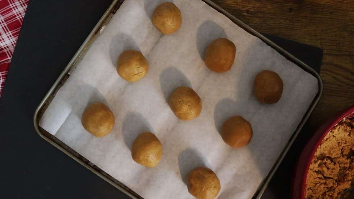 Round balls of peanut butter cookie dough laid out on a parchment lined baking sheet.