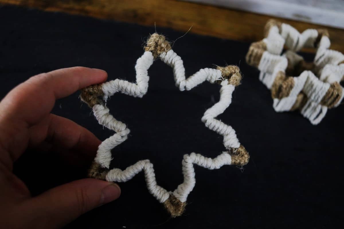 Snowflake shaped ornament with white twine wrapped on it and jute twine in the tips.