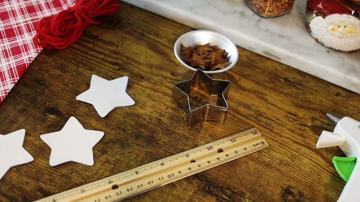 A ruler, star shaped cookie cutter, cardboard stars, and small dish of rustic stars on a wooden surface.