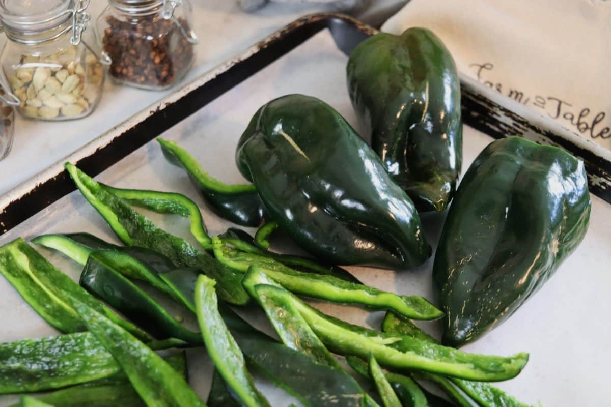 Raw poblano peppers on a parchment lined baking sheet, some are sliced others are whole.