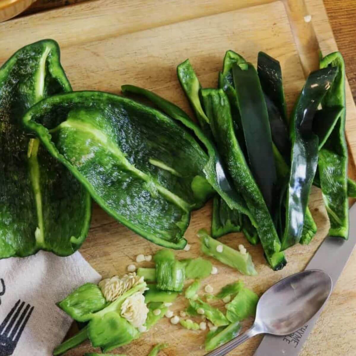 Poblano peppers cut into halves and strips on a wooden cutting board beside a spoon and paring knife.