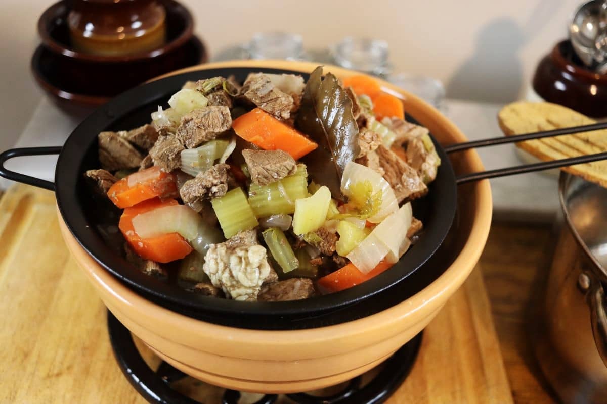 beef and vegetables in a strainer sitting on top of a bowl.