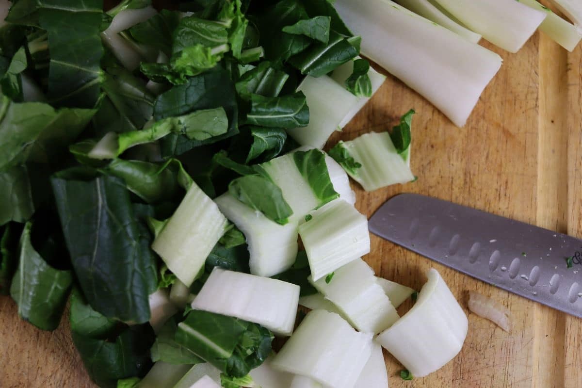 Chopped bok choy on a cutting board with a knife sitting next to it.