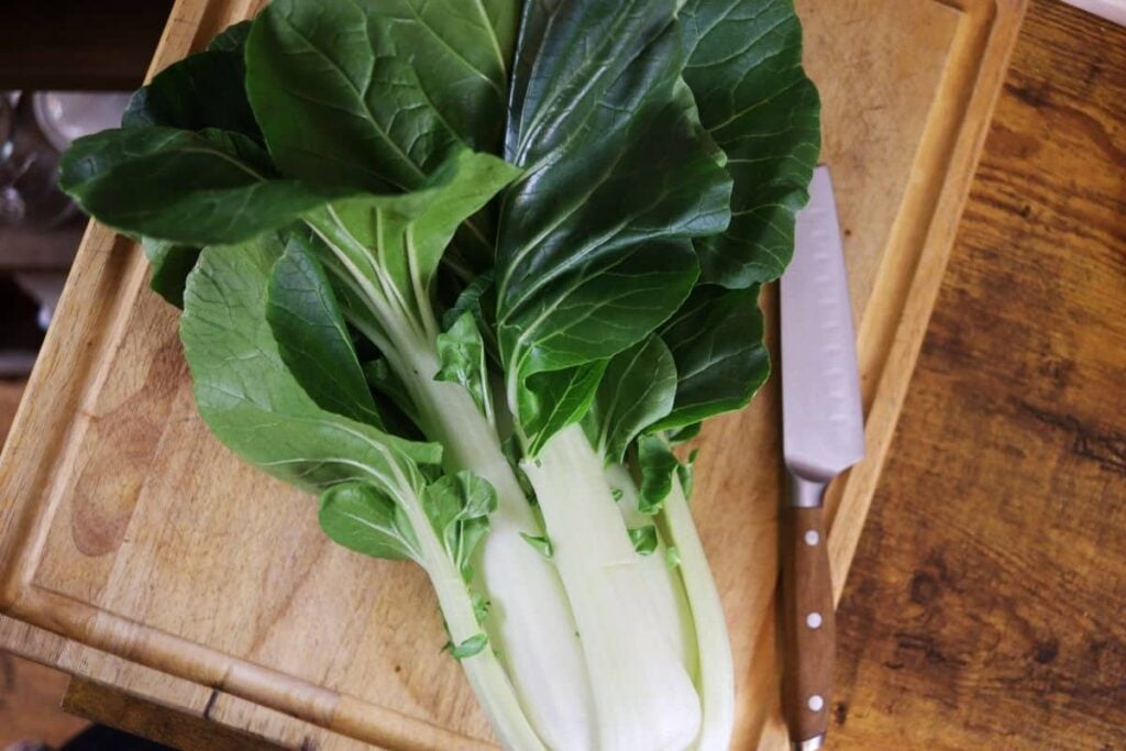 a head of fresh bok choy on a cutting board with a knife