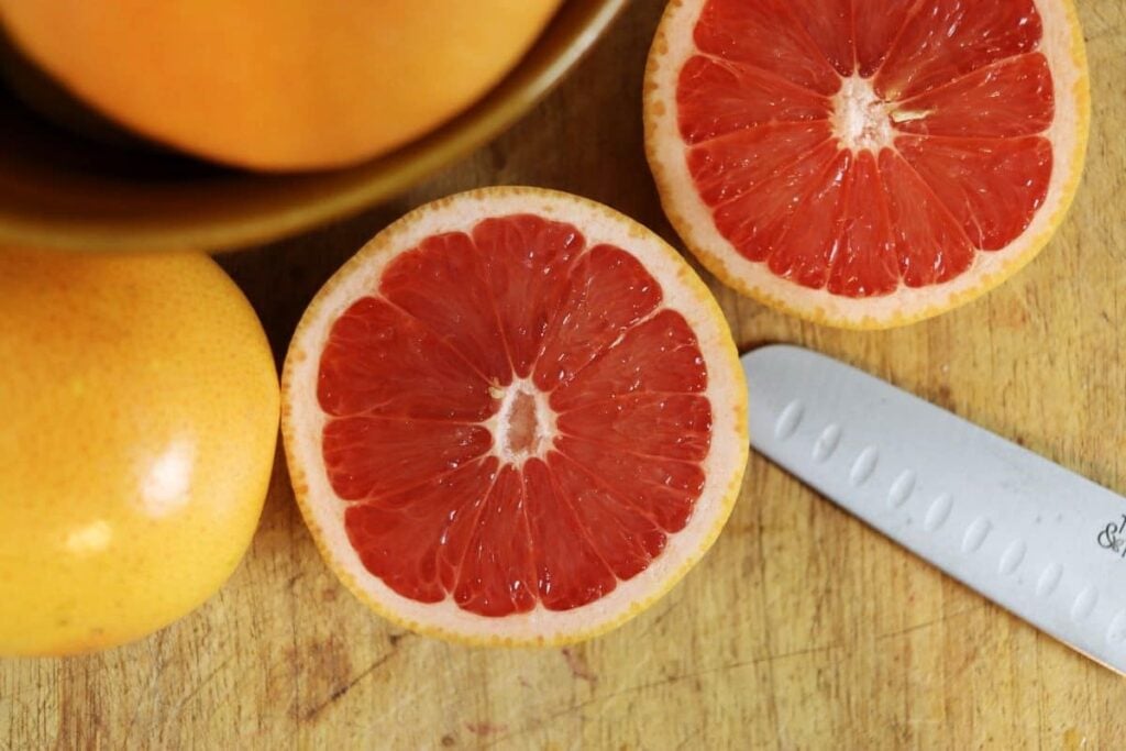 overview of a grapefruit cut in half sitting on a table next to a knife.
