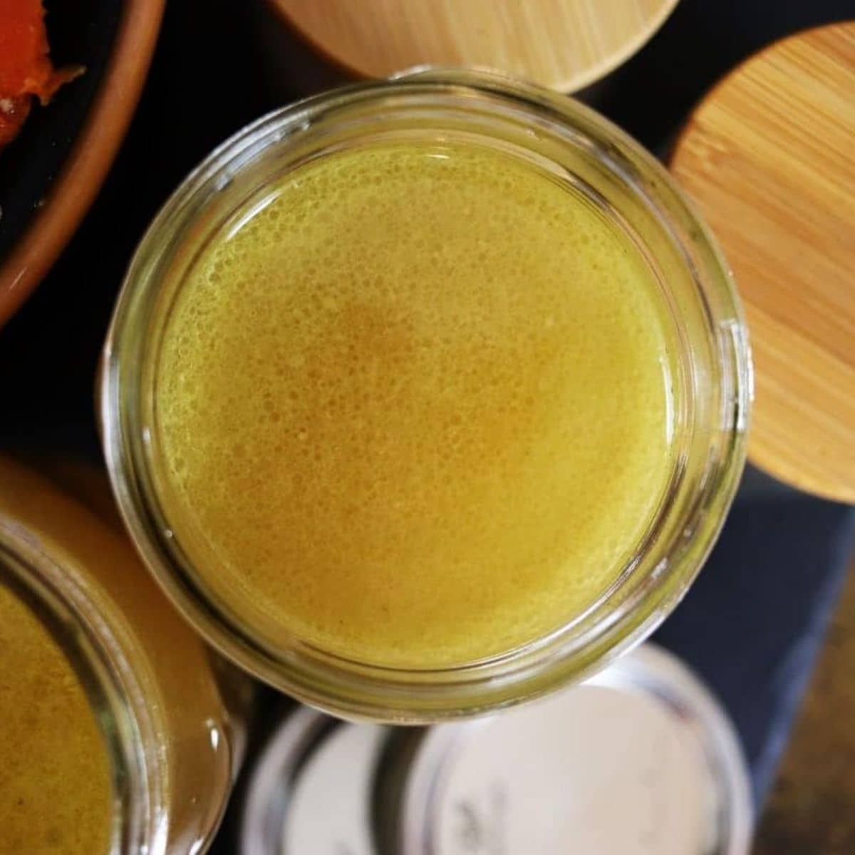 Mason jar of yellow broth with bamboo and metal lids visible next to it.