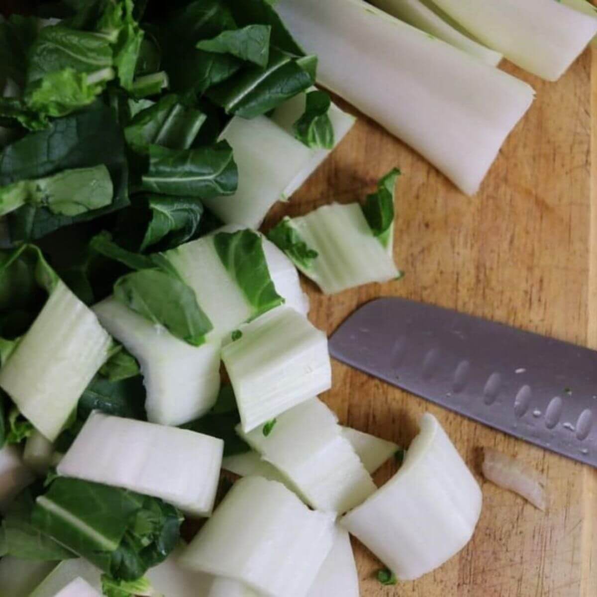 Fresh chopped bok choy scattered across a wooden cutting board with a knife.