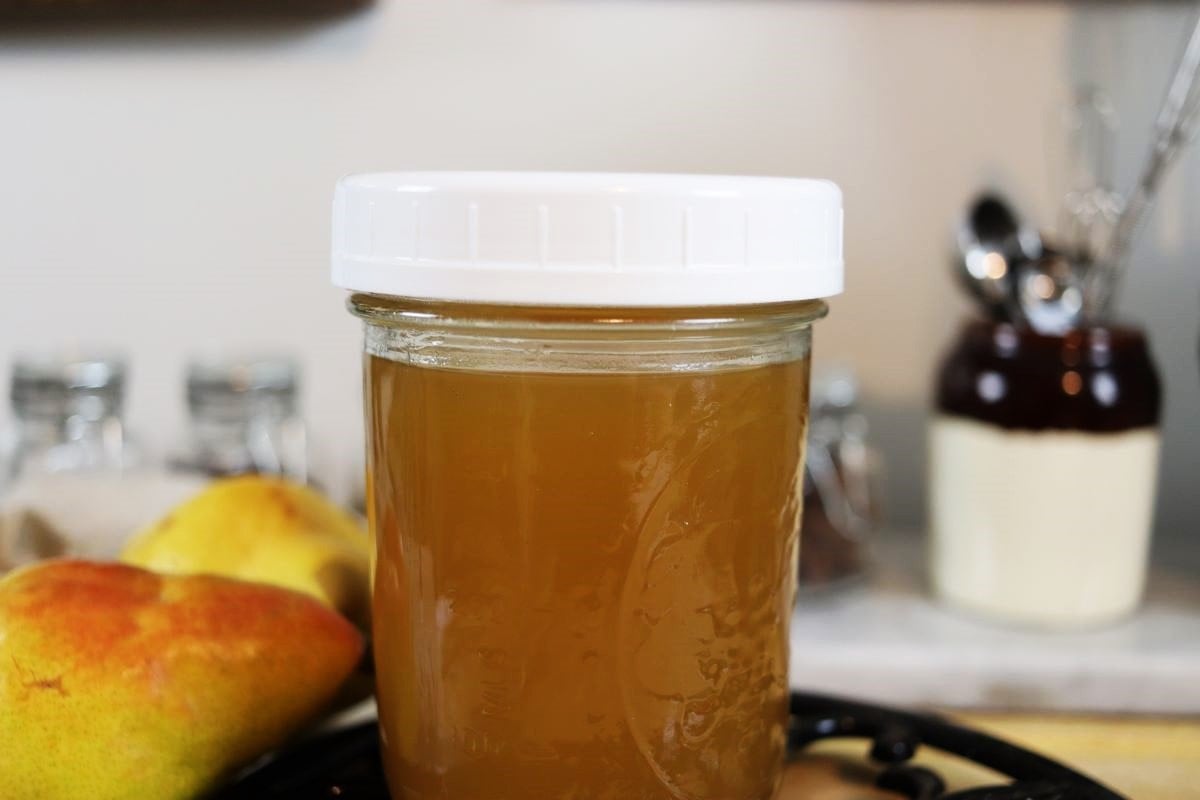 Mason jar of golden liquid with a white lid on it sitting on a counter.