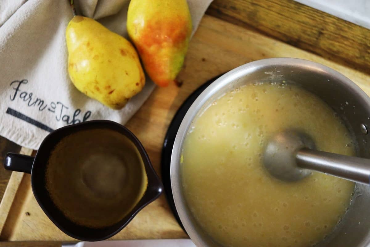 Yellow puree in a saucepan on a counter with pears and a small pitcher visible next to it.