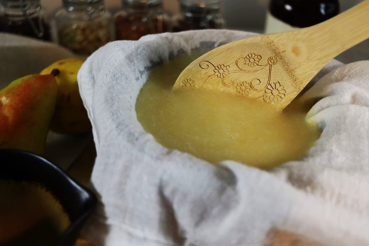 Yellow puree in a flour sack lined strainer with a wooden spoon in it.