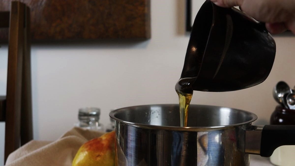 Honey being poured from a small black pitcher into a saucepan.