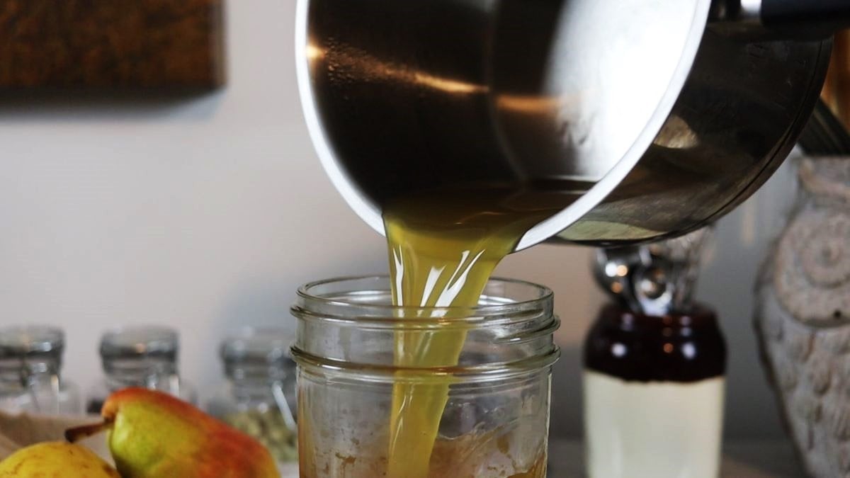 Yellow liquid being poured from a saucepan into a mason jar.
