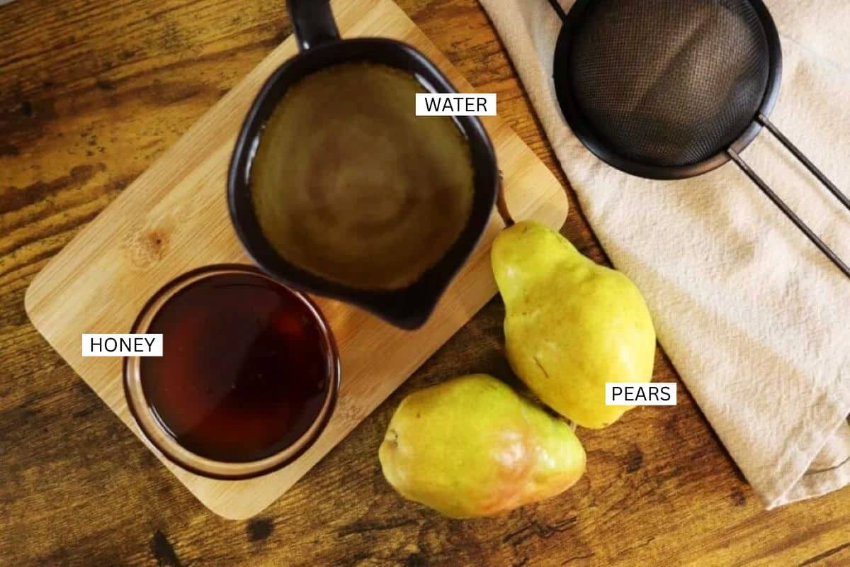 A wooden surface with a cutting board holding a black pitcher of water, a glass bowl of honey, and two yellow pears. A mesh strainer and light cloth are nearby. Items are labeled: water, honey, and pears.