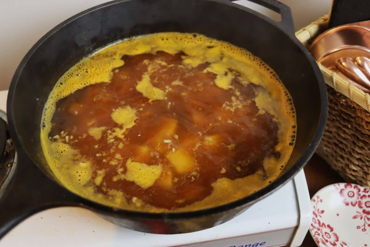 Broth with potatoes visible in it simmering in a cast iroin skillet.