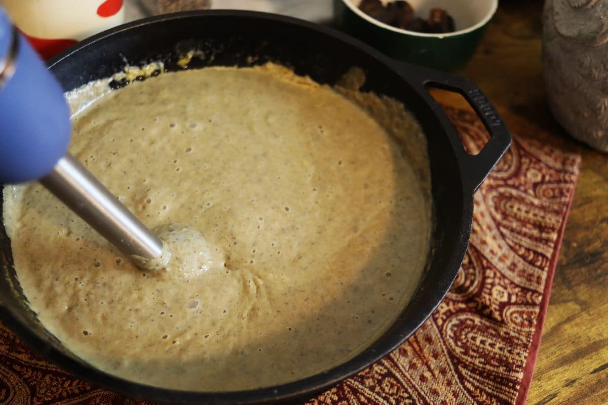 Immersion blender blending creamy mixture in a cast iron skillet.