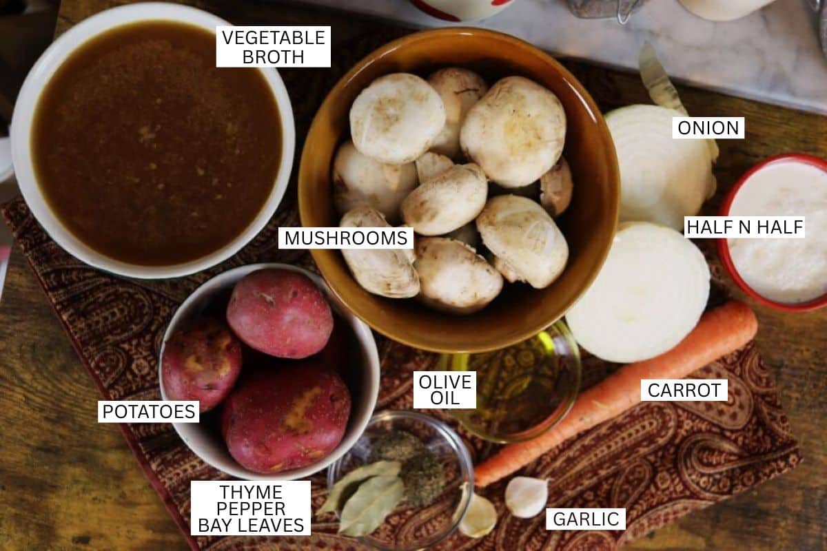 Labeled soup ingredients: vegetable broth, mushrooms, onion, half and half, potatoes, olive oil, carrot, thyme, pepper, bay leaves, and garlic, arranged on a patterned cloth.