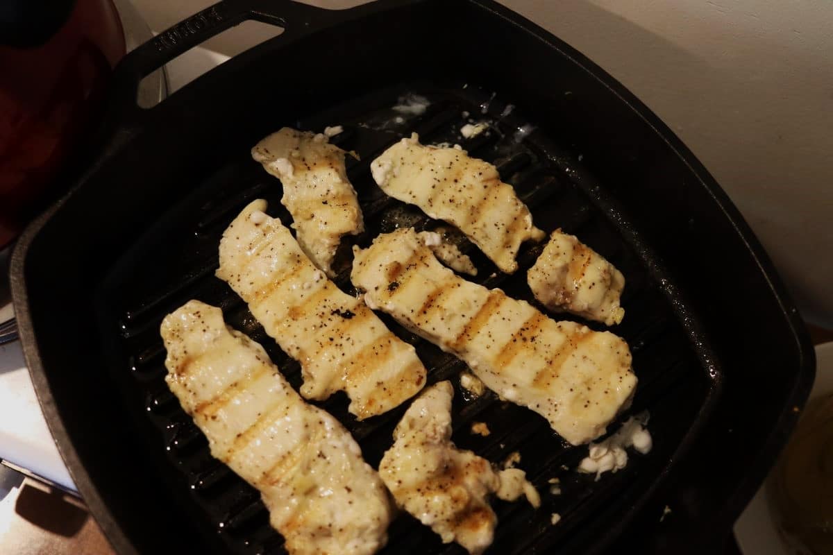 chicken strips cooking in a cast iron grill pan.