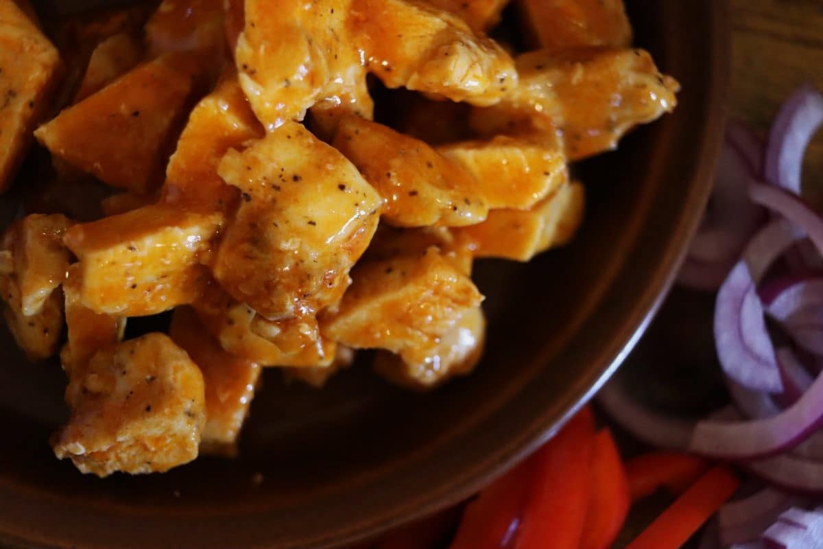 chunks of cooked chicken coated in buffalo sauce on a plate.