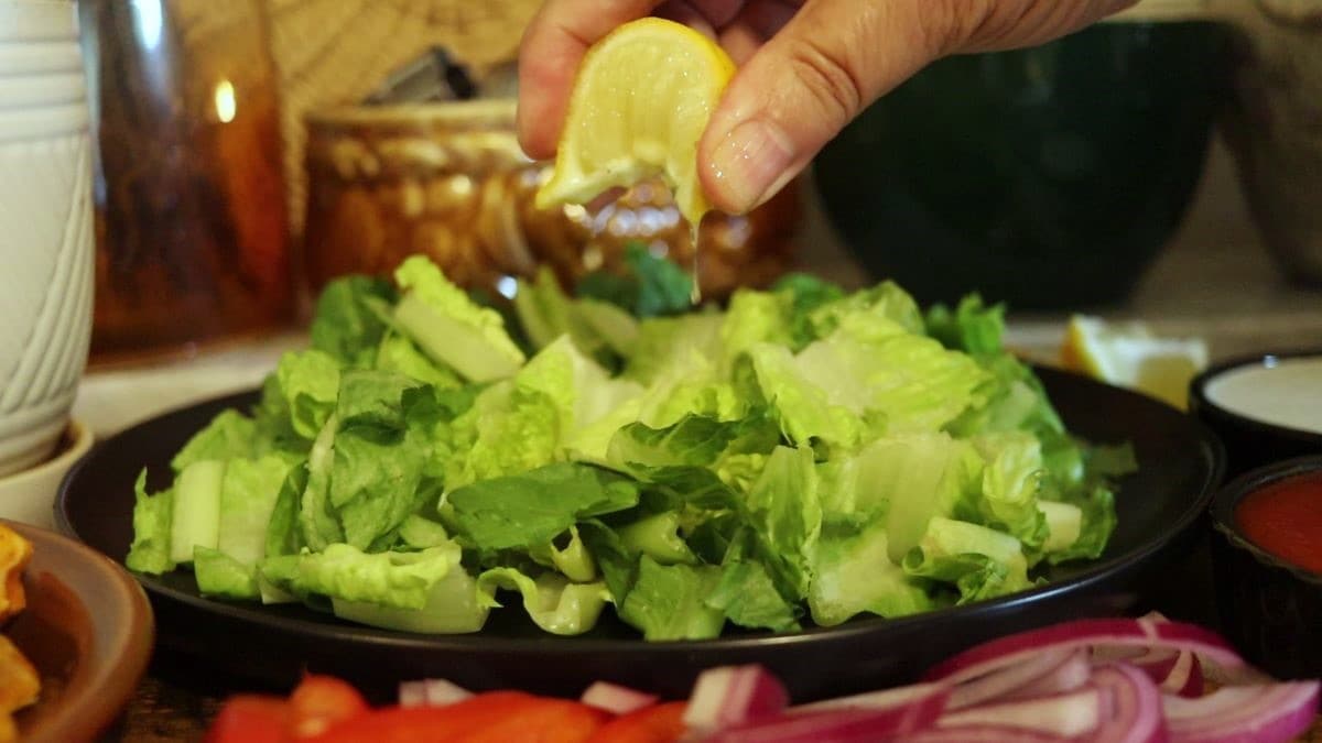 squeezing lemon over a plate of cut up romaine lettuce.