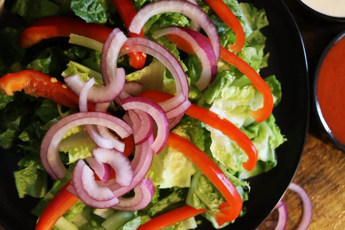 a plate of romaine lettuce topped with sliced red bell pepper and sliced red onion.