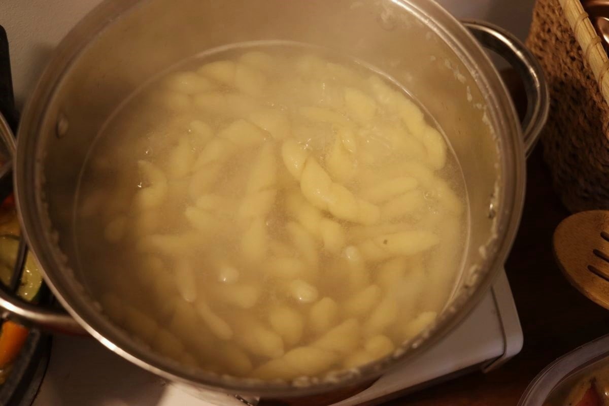 handmade trofie pasta simmering in a pot of water.