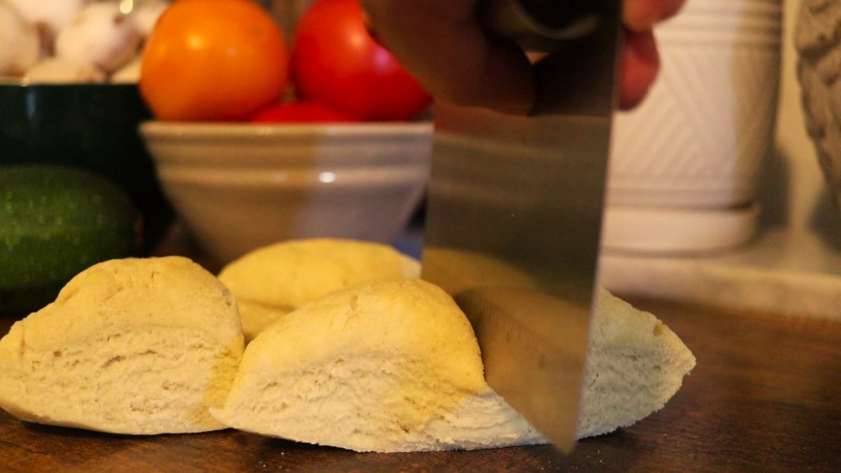 a bench knife cutting a ball of dough into quarters.