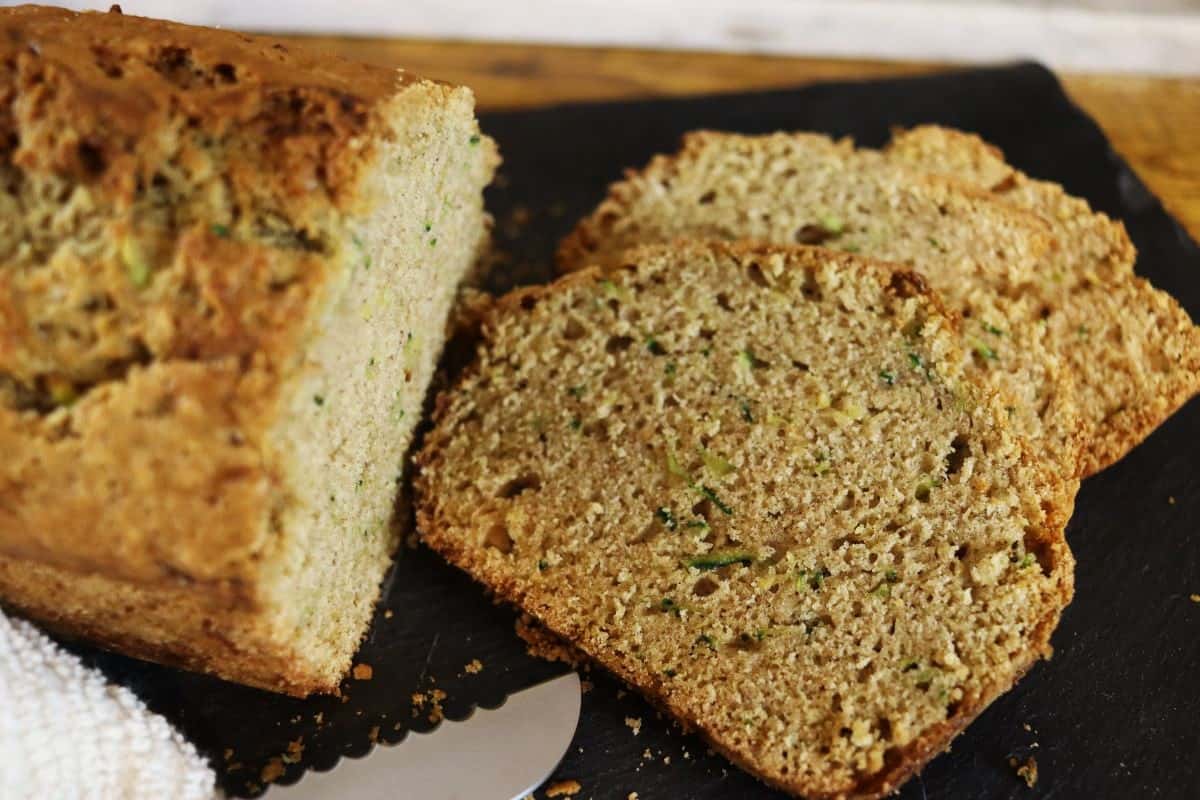 Slices of zucchini bread cut from the loaf sitting next to them with a knife visible in front.