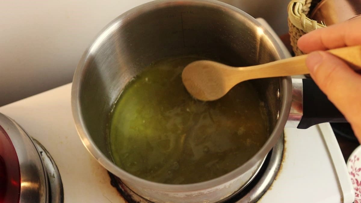 stirring oil and chicken broth in a saucepan with a wooden spoon.