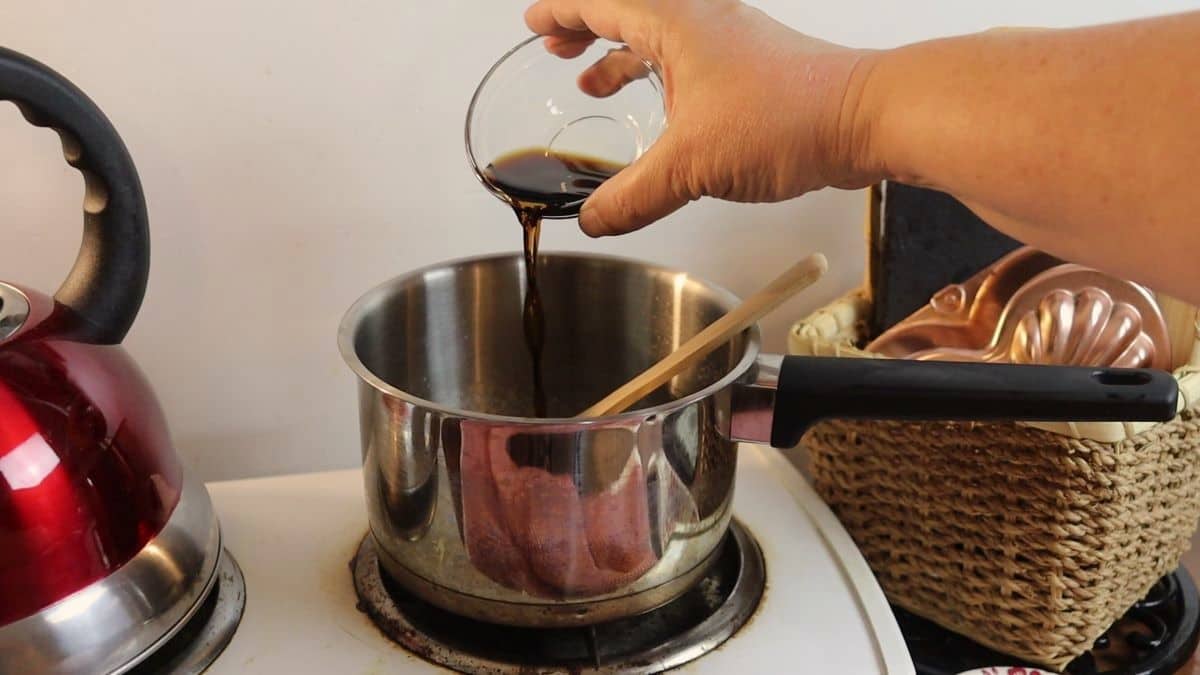 pouring liquid aminos into a saucepan sitting on a stovetop.