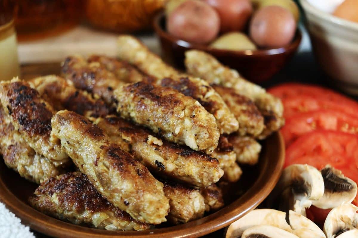 Cooked sausage links piled on a plated with a bowl of potatoes visible in the background.