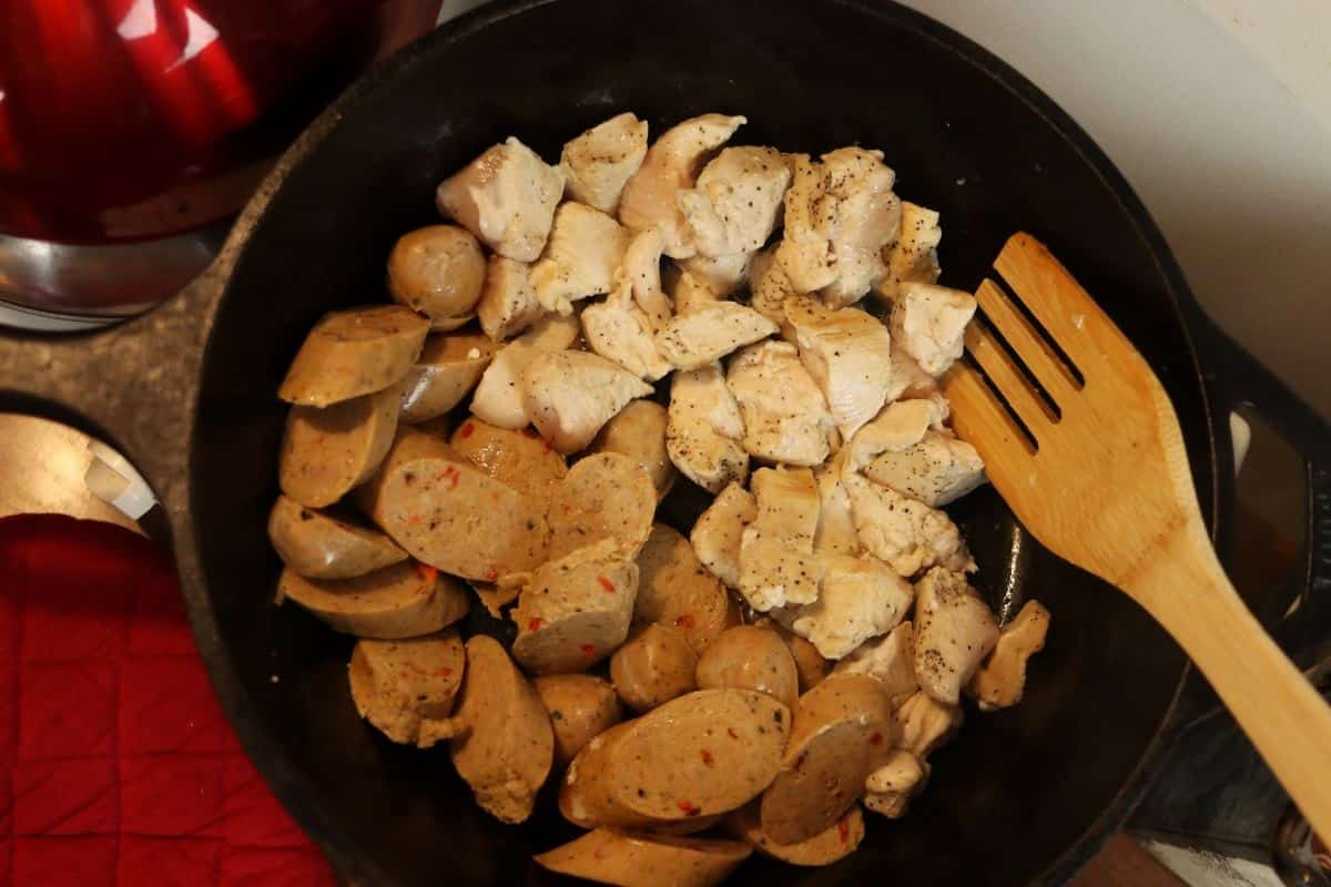 Chunks of chicken and chicken sausage sauteing in a skillet.