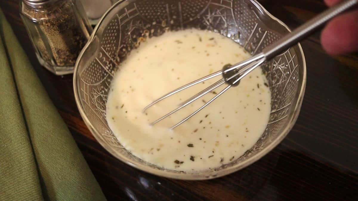 White sauce with seasoning in it in a small bowl with a whisk sitting in it.