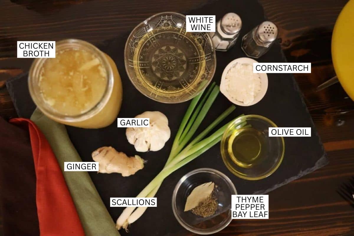 A slate board displays labeled ingredients: chicken broth, white wine, cornstarch, olive oil, garlic, ginger, scallions, thyme, pepper, and a bay leaf, with a salt and pepper shaker on the side.
